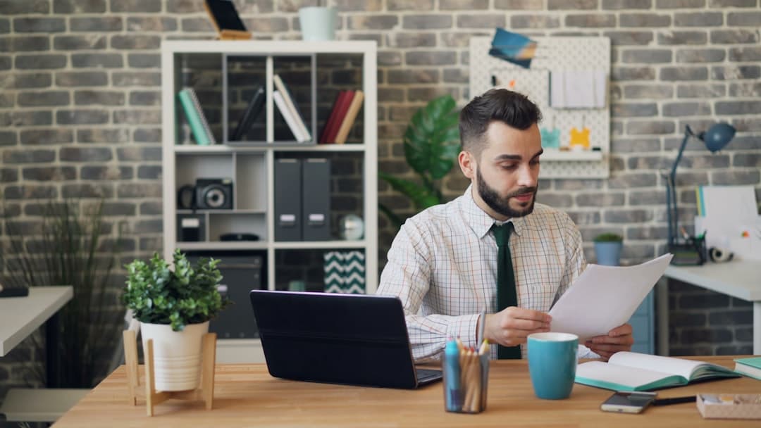Business owner reviewing contractor payment documents at desk with calculator and paperwork