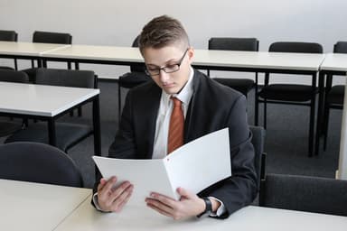 Business professional reviewing contractor documents at desk with laptop and paperwork